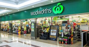 Un magasin Woolworths avec une enseigne verte, des présentoirs promotionnels et une zone de caisses.