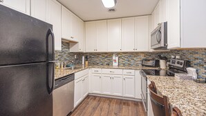 A kitchen with white cabinets, a black refrigerator, a microwave, and a tiled backsplash. - Uptown OC 2 Bedroom | Pool, Sauna & Pickleball (Ocean City)