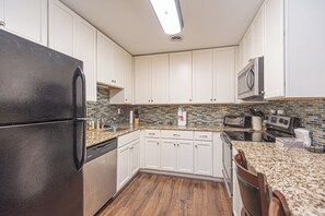 A kitchen with white cabinets, a black refrigerator, a microwave, and a tiled backsplash. - Uptown OC 2 Bedroom | Pool, Sauna & Pickleball (Ocean City)