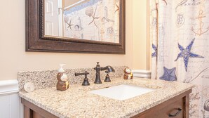 A bathroom with a granite countertop, a sink, a mirror, a towel dispenser, and a wooden cabinet. - Uptown OC 2 Bedroom | Pool, Sauna & Pickleball (Ocean City)