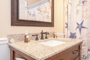A bathroom with a granite countertop, a sink, a mirror, a towel dispenser, and a wooden cabinet. - Uptown OC 2 Bedroom | Pool, Sauna & Pickleball (Ocean City)
