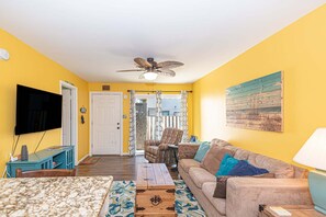 A living room with a television, sofa, coffee table, and a ceiling fan. - Uptown OC 2 Bedroom | Pool, Sauna & Pickleball (Ocean City)