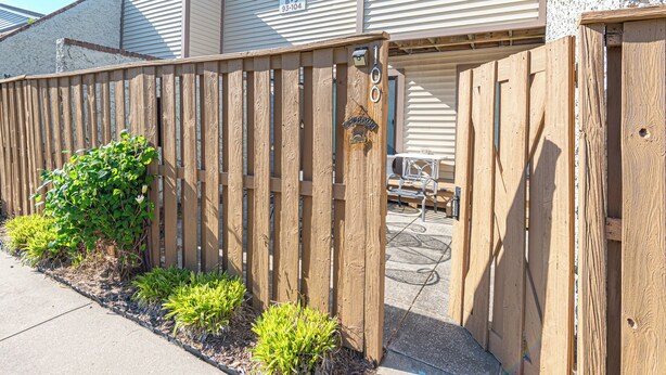 A wooden fence with a mailbox and a welcome sign, a paved driveway, and a building with a garage door. - Uptown OC 2 Bedroom | Pool, Sauna & Pickleball (Ocean City)