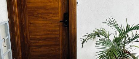 Una puerta de madera con un cartel encima, un felpudo y una planta en maceta al lado de la puerta.