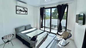 Un dormitorio moderno con cama, una mesita, una silla y un amplio ventanal con cortinas.