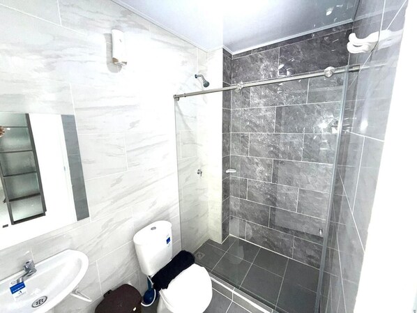Un baño con ducha, inodoro, lavabo y secamanos.