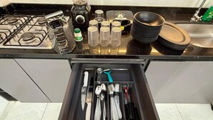 Una cocina con estufa a gas, licuadora y varios utensilios y vajilla organizados.