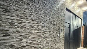 Un edificio moderno con fachada de piedra texturizada, una puerta metálica y un macetero con flores.