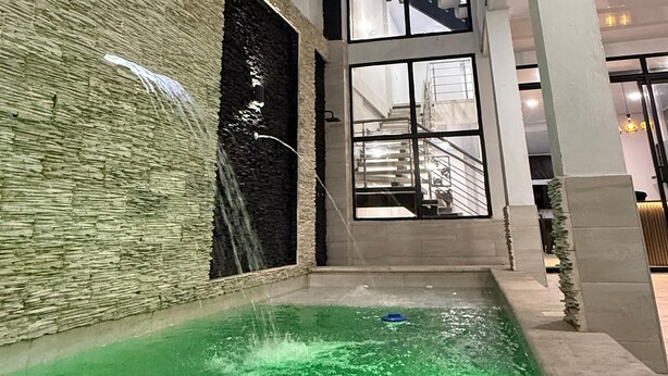 Un edificio moderno con fachada de vidrio, una pequeña piscina al aire libre con agua verde y un muro de piedra en un lateral.