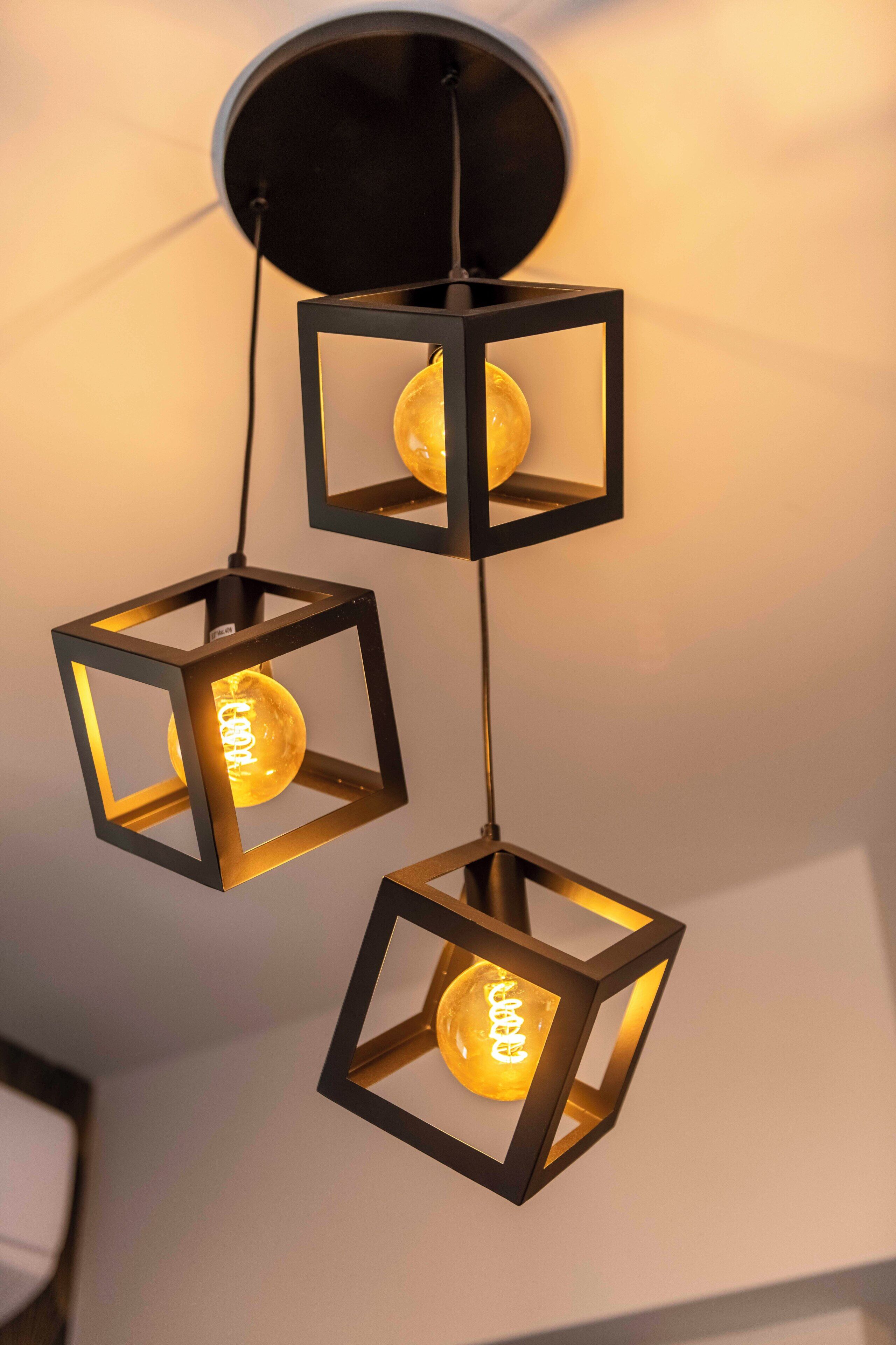 A modern chandelier with three square frames, each containing a glowing bulb.