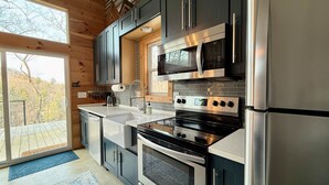 A modern kitchen with stainless steel appliances, grey cabinets, and a large window overlooking a deck.