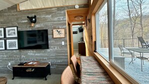 A modern interior with a large window, a wooden bench, a flat-screen TV, and a stone wall.