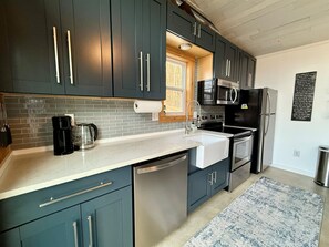 A modern kitchen with dark cabinets, stainless steel appliances, and a white countertop. - Wrigs Ridge | Tiny Cabin w/ Views & Creek Sound (Robbinsville)