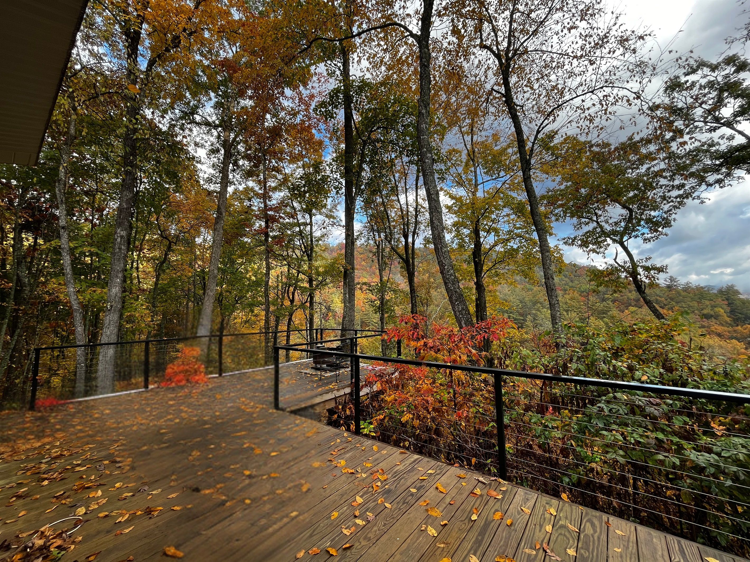 Eine Holzterrasse mit Metallgeländer mit Blick auf ein bewaldetes Gebiet im Herbstlaub.