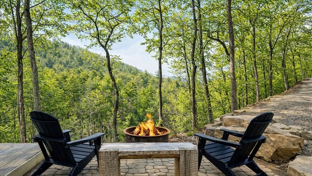 An outdoor seating area with two Adirondack chairs, a stone fire pit, and a wooden table.