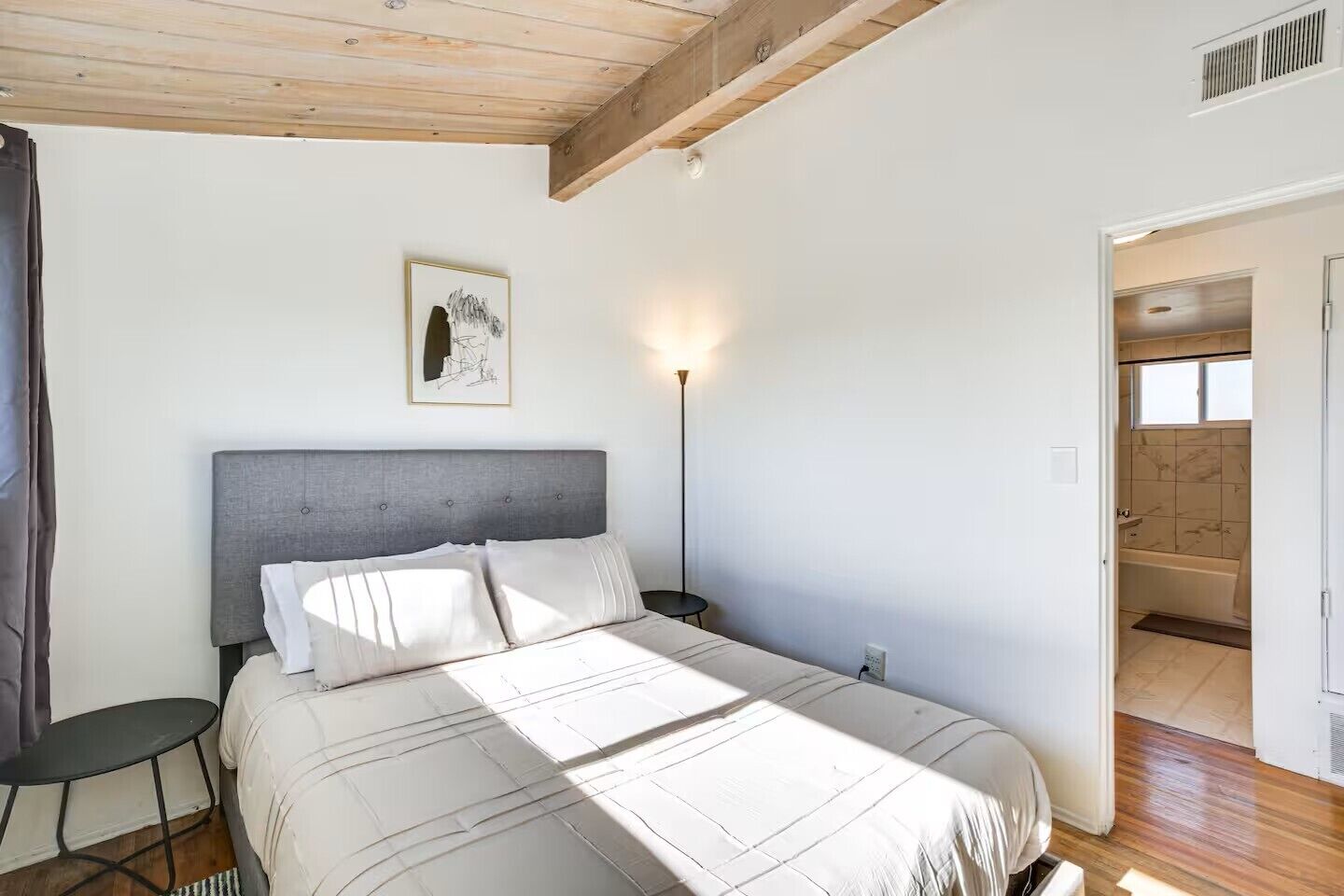 A bedroom with a bed, bedside table, and a nightstand. There is a window and a door leading to another room.