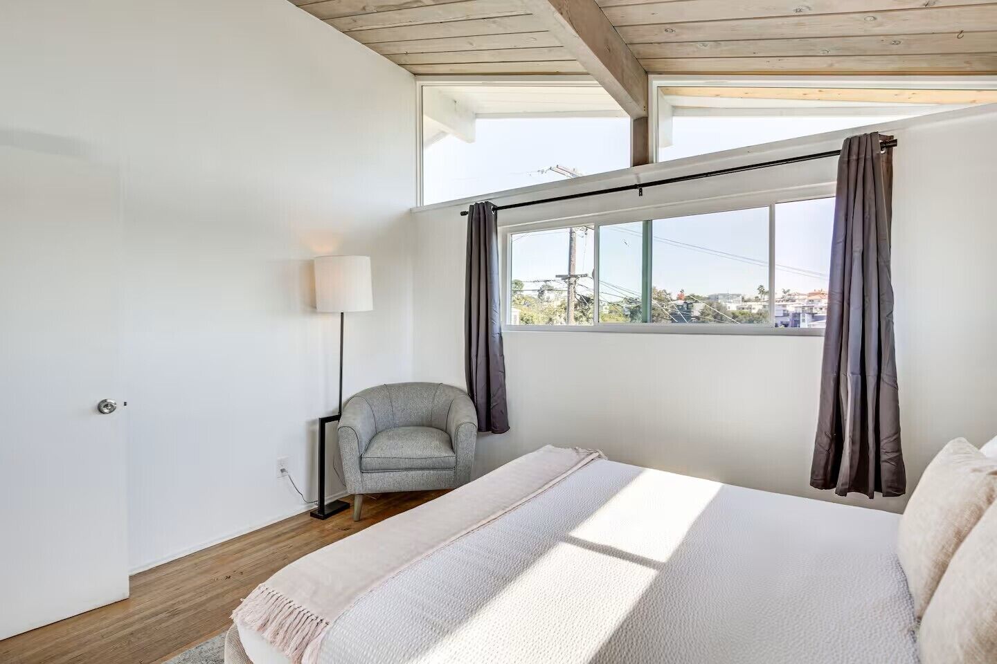 Un dormitorio con cama, una silla, una lámpara y una ventana con cortinas.