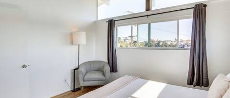 Un dormitorio con cama, una silla, una lámpara y una ventana con cortinas.