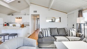 A modern living room with a grey sofa set, a small white table, and a kitchen area with white cabinets and a countertop. - 3 bedroom condo with expansive view (San Diego)