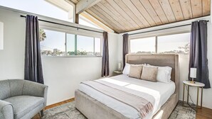 A bedroom with a large bed, a chair, and a view of the city through large windows. - 3 bedroom condo with expansive view (San Diego)