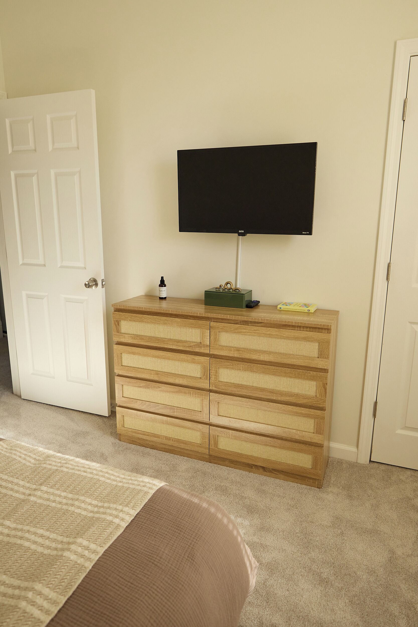 A room with a wooden dresser, a flat-screen TV mounted on the wall, and a door.
