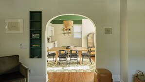 Un comedor con una mesa y sillas de madera, una lámpara colgante de fibra natural y un arco verde que da a la cocina.