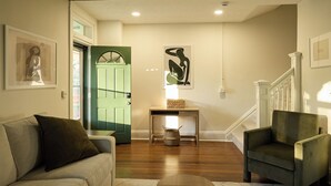 Una sala de estar con una puerta verde, un sofá, una silla, una mesita y una escalera.