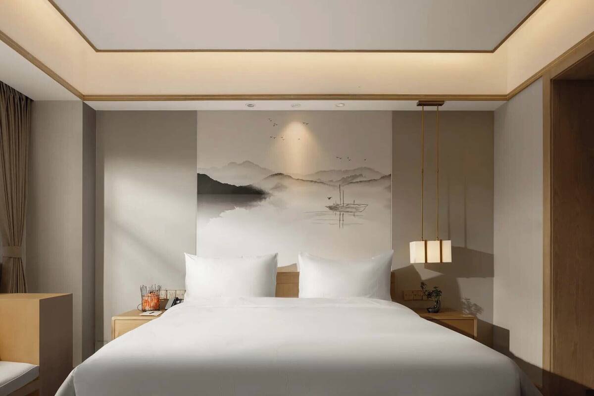 A hotel room with a large bed, a nightstand, a lamp, and a wall painting.