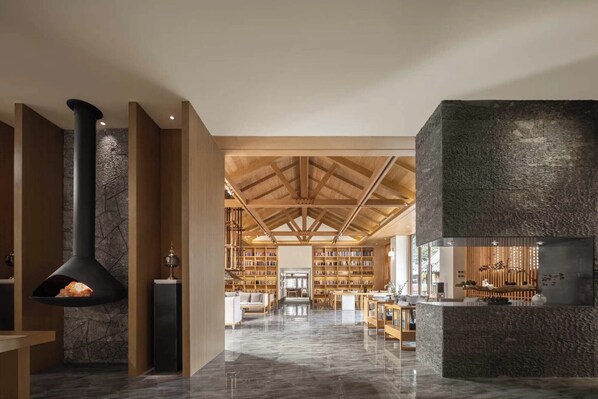 A spacious library with high ceilings and wooden beams, featuring a fireplace and a stone accent wall. - GF Healing Hotel & Resort (Lijiang)