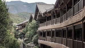Un bâtiment traditionnel en bois, doté de nombreux balcons et de grandes fenêtres, entouré d’une végétation luxuriante et avec des montagnes en arrière-plan.