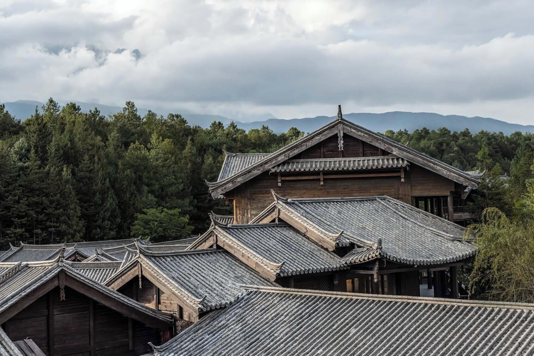 A traditional wooden building with multiple roofs and a mountainous backdrop.