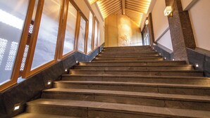 Un escalier avec des rampes en bois et des marches en pierre, menant à une pièce dotée d’un haut plafond et d’un mur en pierre.