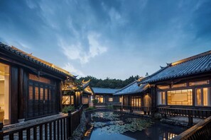 A traditional courtyard with tiled roofs and wooden buildings, a pond with lily pads, and a wooden fence. - GF Healing Hotel & Resort (Lijiang)