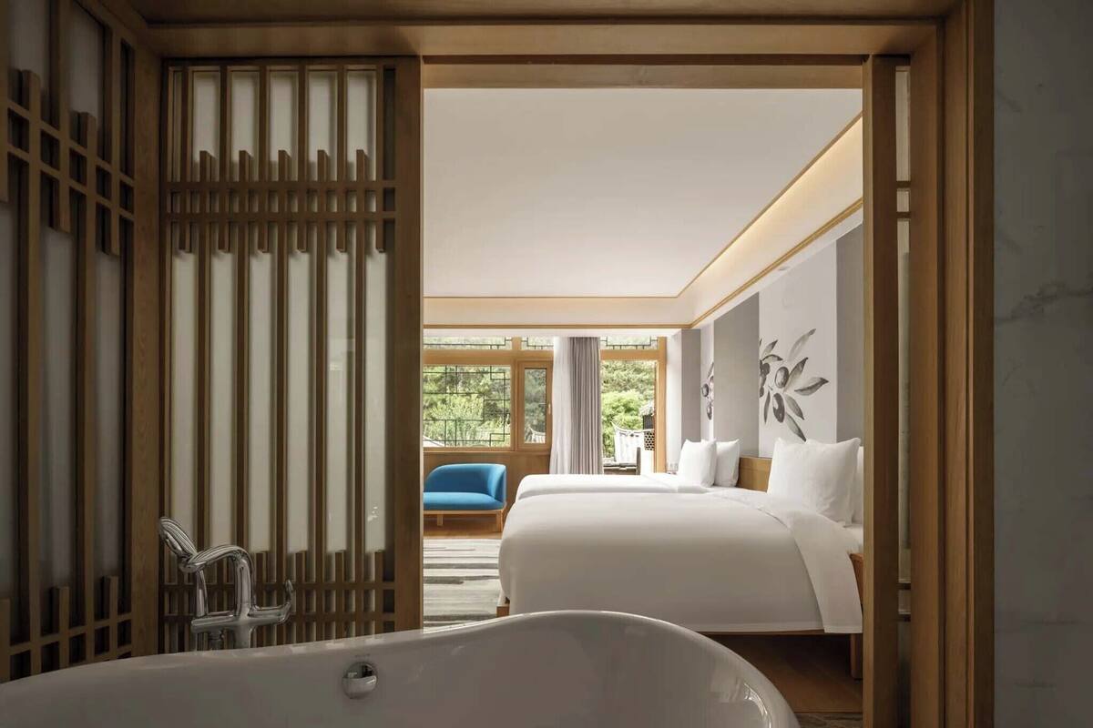 A modern hotel room with a large bathtub, two beds, and a view of the outdoors.
