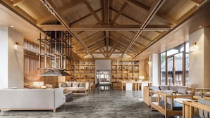 Une bibliothèque spacieuse avec de hauts plafonds et des poutres en bois, comprenant des étagères, des coins lecture et un escalier central.