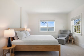 A bedroom with a bed, bedside lamps, a chair, a window with a view of the sea, and a small table. - Private Oceanfront Oasis 4-bedroom house in Brooklin perfect for your getaway (Brooklin)