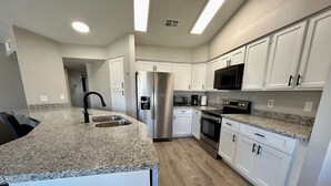 Une cuisine moderne avec des armoires blanches, des comptoirs en granit, des appareils en acier inoxydable et un plancher en bois.