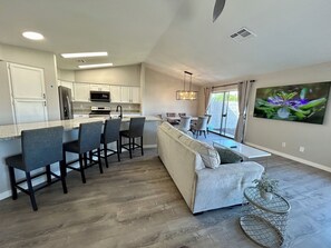 A modern kitchen with a central island, bar stools, a dining area with a sofa, and a large window with a view. - Ahwatukee Gem: Pool ,Hot Tub, Mini-Golf, Bocce (Phoenix)