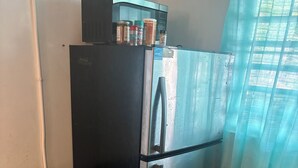 Une cuisine équipée d’un réfrigérateur en acier inoxydable, d’un four à micro-ondes placé au-dessus, d’un plan de travail avec une plaque de cuisson, de placards en bois et d’une poubelle.