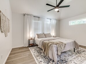 A bedroom with a bed, bedside tables, a ceiling fan, and a window with curtains.