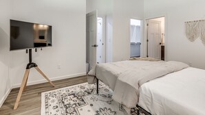 Een slaapkamer met een bed, een televisie op een driepotige standaard, een plafondventilator en een kamerkleed met een patroon.