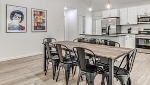 Een moderne keuken met witte kasten, roestvrijstalen apparatuur en een houten eettafel met stoelen.