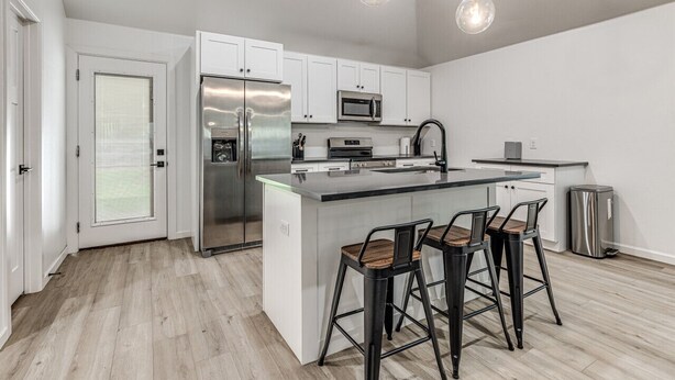 Een moderne keuken met witte kastjes, roestvrijstalen apparatuur en een centraal eiland met barkrukken.