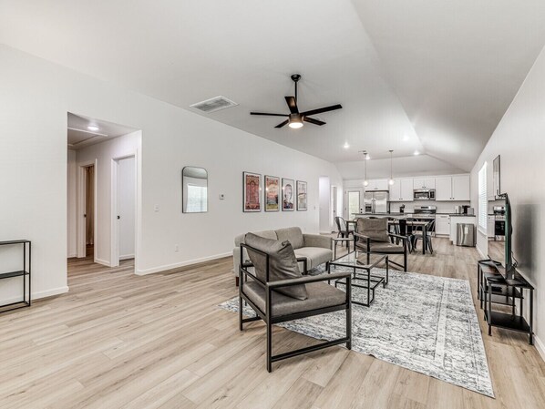A spacious living area with a high ceiling, a ceiling fan, and a dining area with a kitchen in the background.