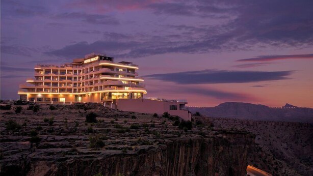 Un hotel de varios pisos con balcones, ubicado en terreno rocoso con vista a un cañón.