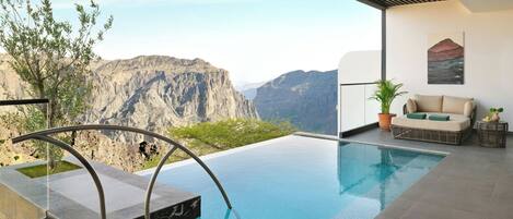 An infinity pool with a view of mountains, a sofa, and a potted plant.