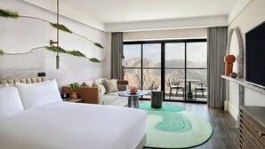 Una habitación de hotel moderna con una cama grande, un sofá, un comedor con mesa y sillas, y un televisor.