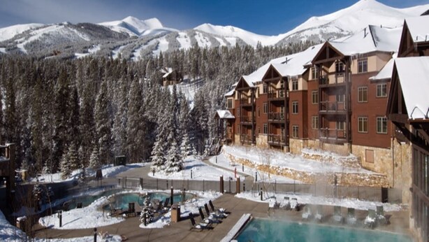 Un resort con zona de piscina, pista de esquí y montañas nevadas al fondo.
