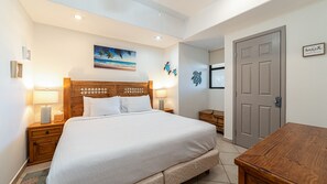 Ein Schlafzimmer mit einem Bett, Nachttischen, einer Holzkommode, einer Tür und einer Wand mit einem Gemälde und einem Schild.