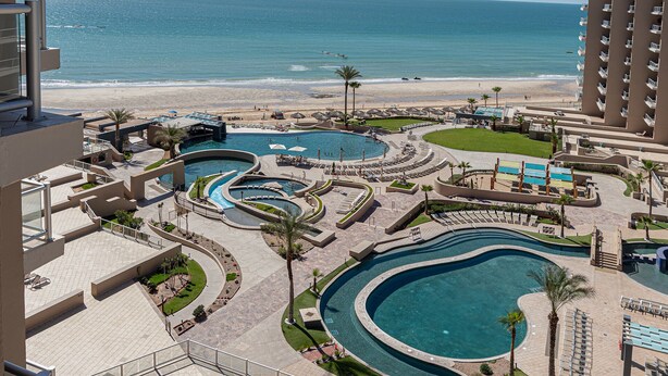 Ein Resort mit mehreren Schwimmbecken, einem Strand und Blick aufs Meer.